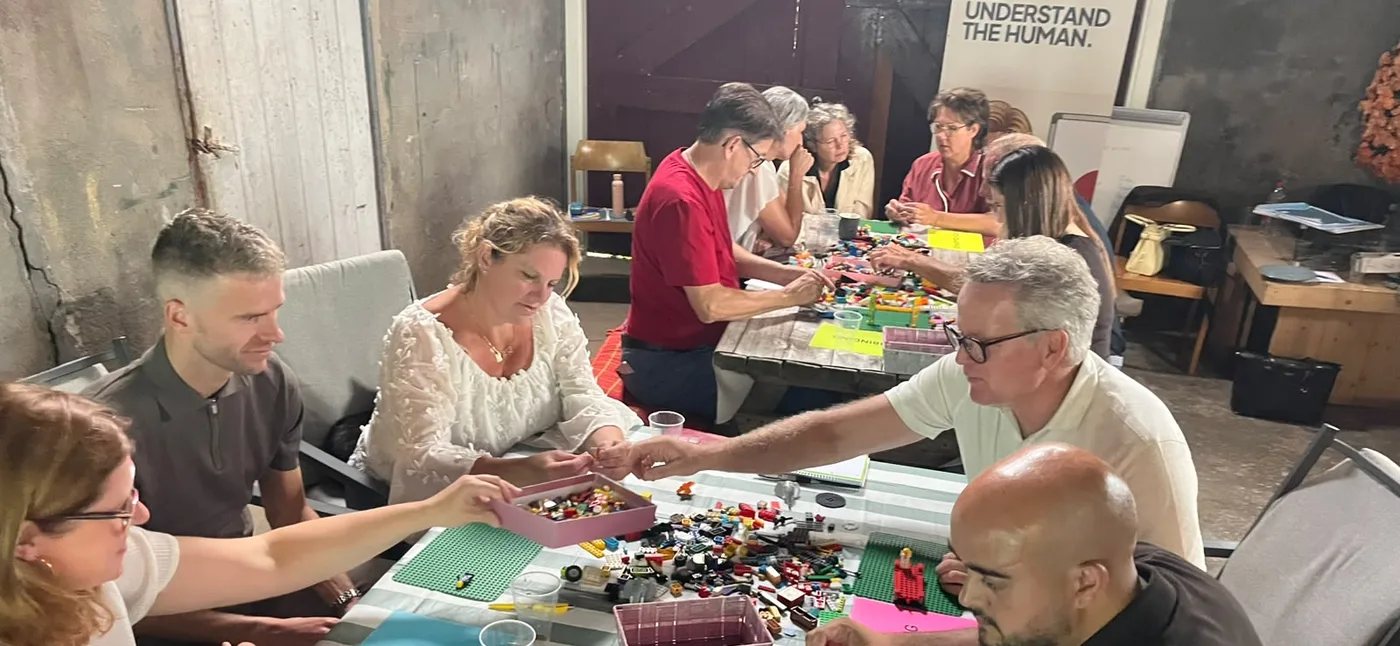 Deelnemers aan de HBG-partnerdag bouwen aan een lange tafel vol LEGO-stenen, ieder aan een eigen bouwwerk